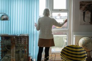 A woman stands with her back to the camera looking out of a window.