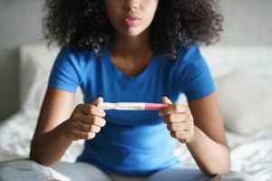 A woman in a blue T-shirt holds a pregnancy test.