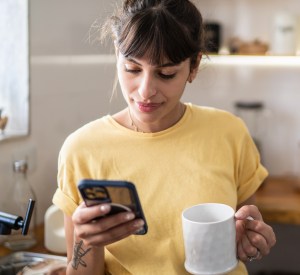 A young woman checks her phone while drinking coffee