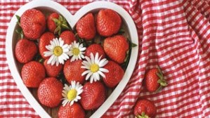 A heart-shaped dish filled with strawberries on a chequered tablecloth.